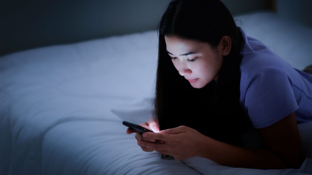 young woman lying on the bed using phone during night time.