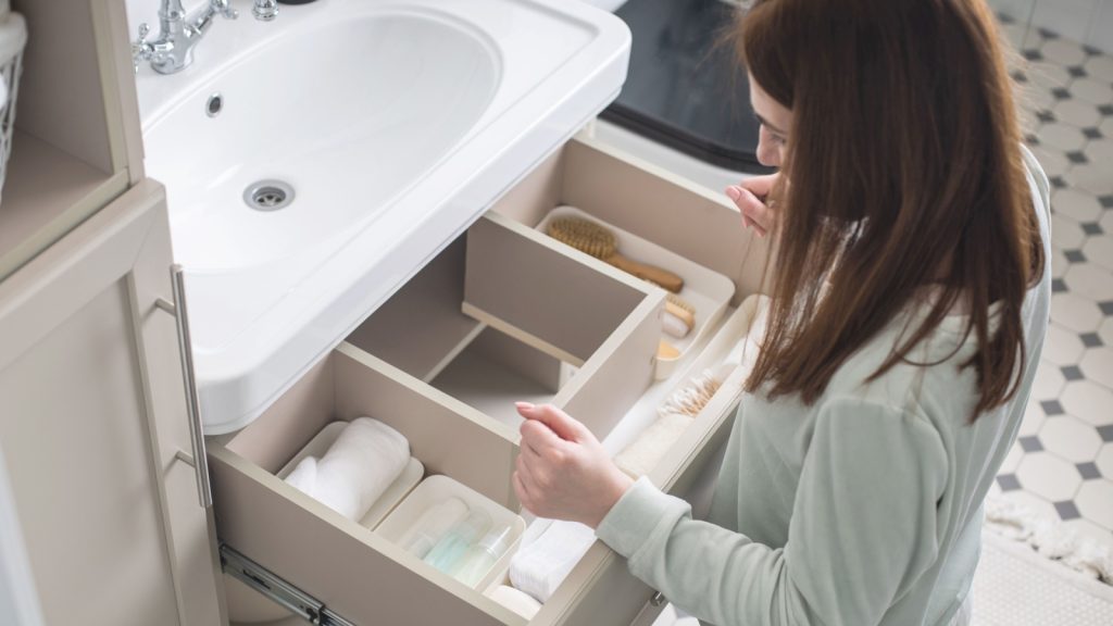 a woman organizing bathroom amenities in open drawer under sink