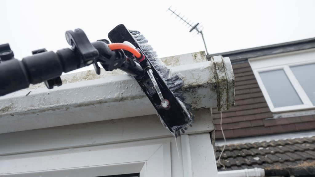 a brush cleaning dirty clogged white plastic pvc gutters and drain pipes with mossy green mould