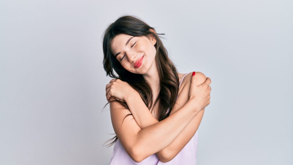 Young girl hugging oneself happy and positive