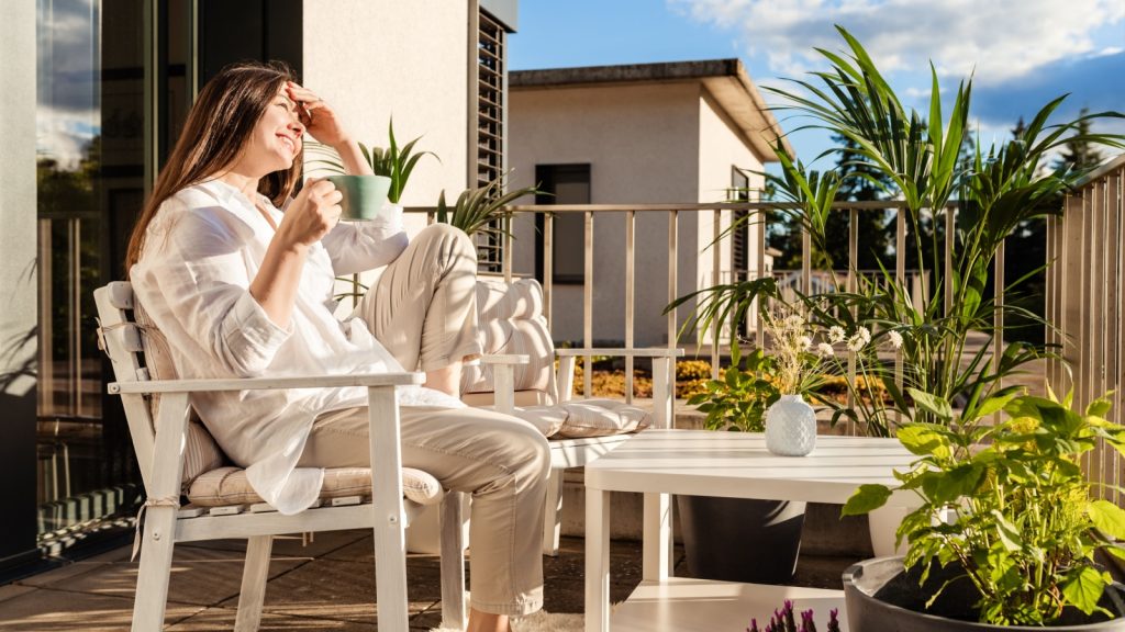 young girl relaxing, drinking tea and enjoying sun sitting at balcony