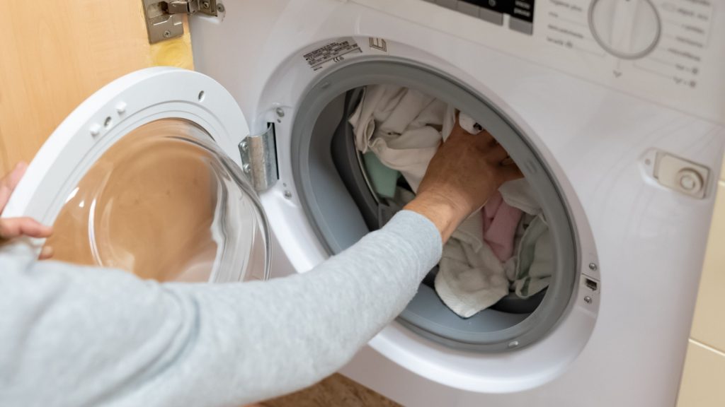 Woman's arm filling the washing machine drum.