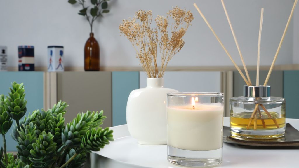 scented candle on white metal table with ceramic vase and reed diffuser