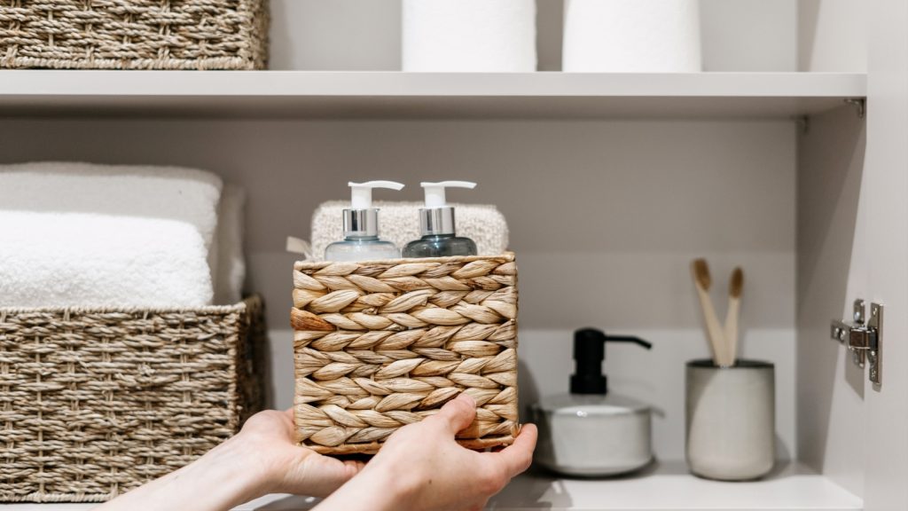 woman putting wicker box with bathroom products inside to organize bathroom cabinet