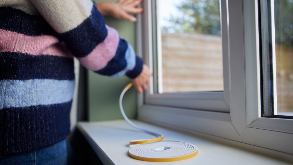 Woman Saving Enegy Insulating Home Putting Draught Excluder Tape On Window.