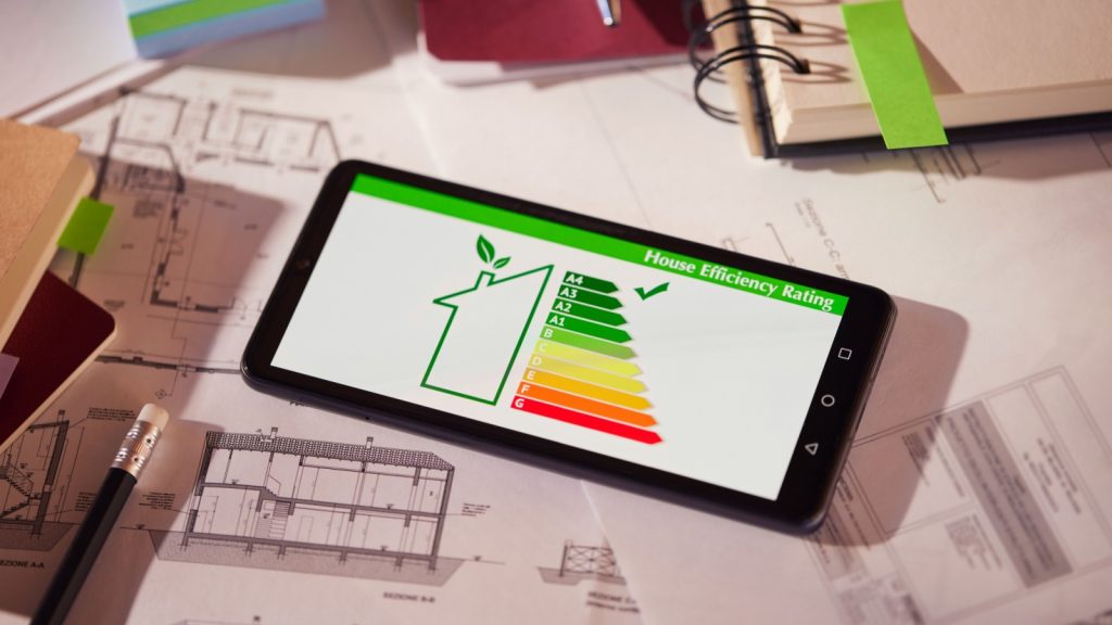 Energy efficiency screen on cellphone leaning on drawings and blueprints of a new house.