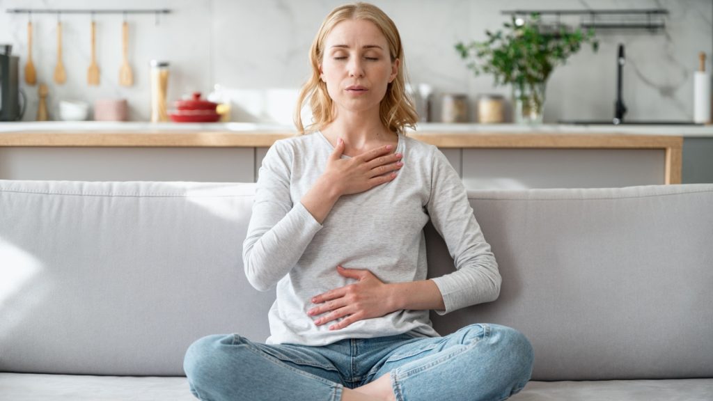 Woman sitting on couch and doing calming breathing exercises