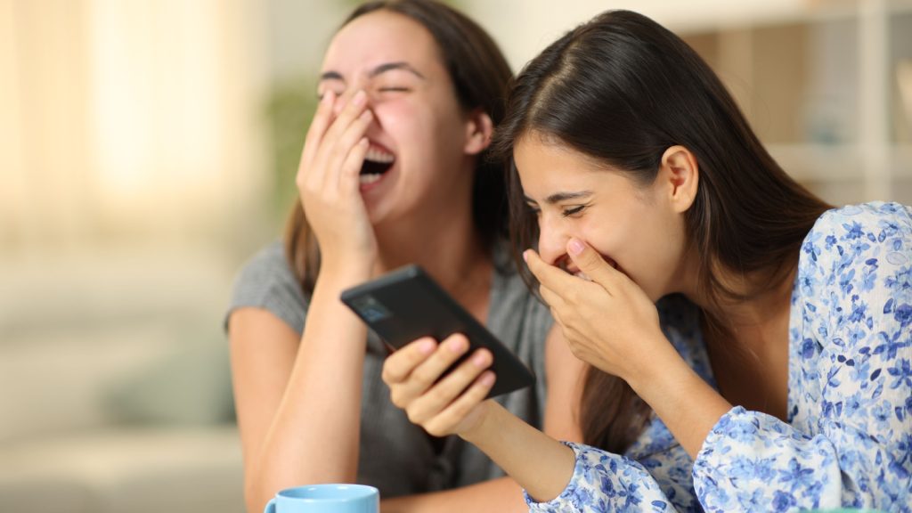 funny friends watching media on their phones, laughing loudly at home