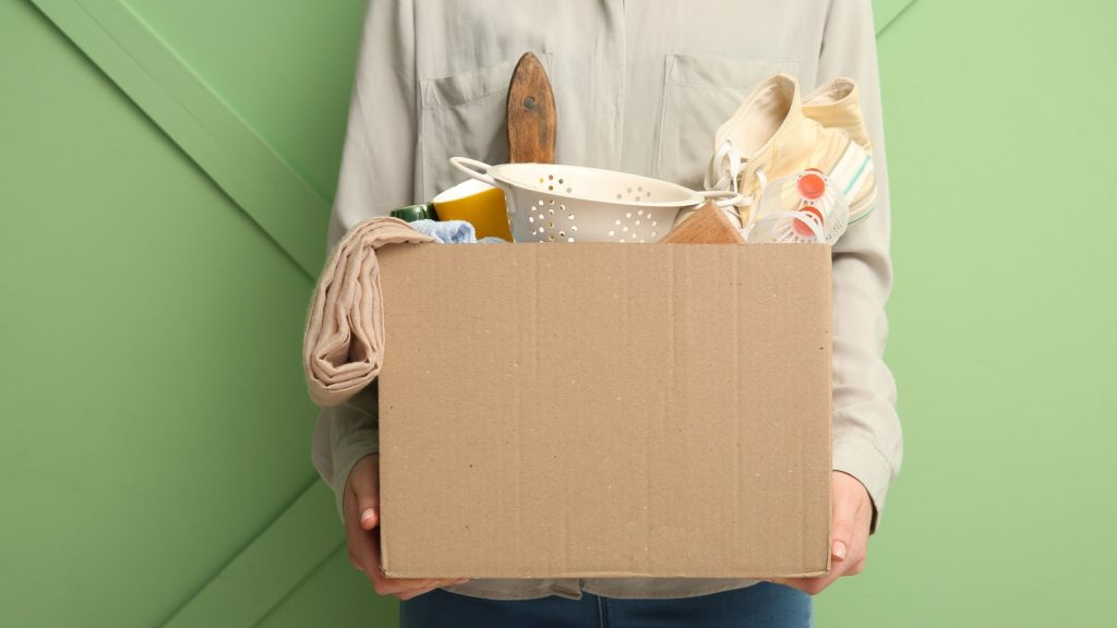 Woman holding box of unwanted stuff for yard sale on green background