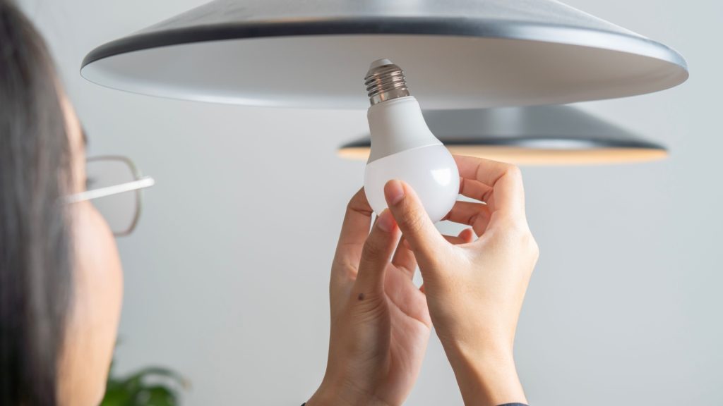 Back view shot of Asian woman changing light bulb to LED at home.