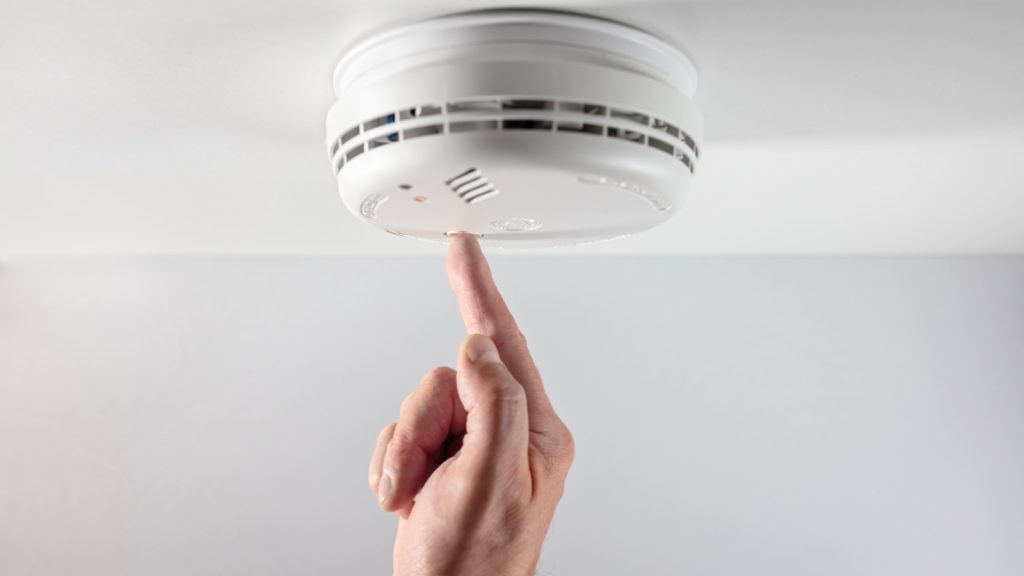 a smoke detector on a ceiling with a man pushing button