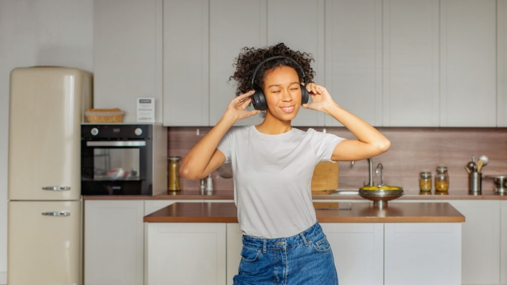 joyful African American woman wearing headphones on dances happily