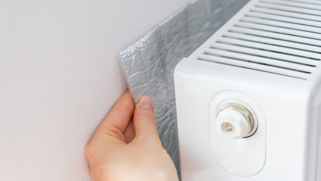 Hand installing thermal insulation behind radiator.