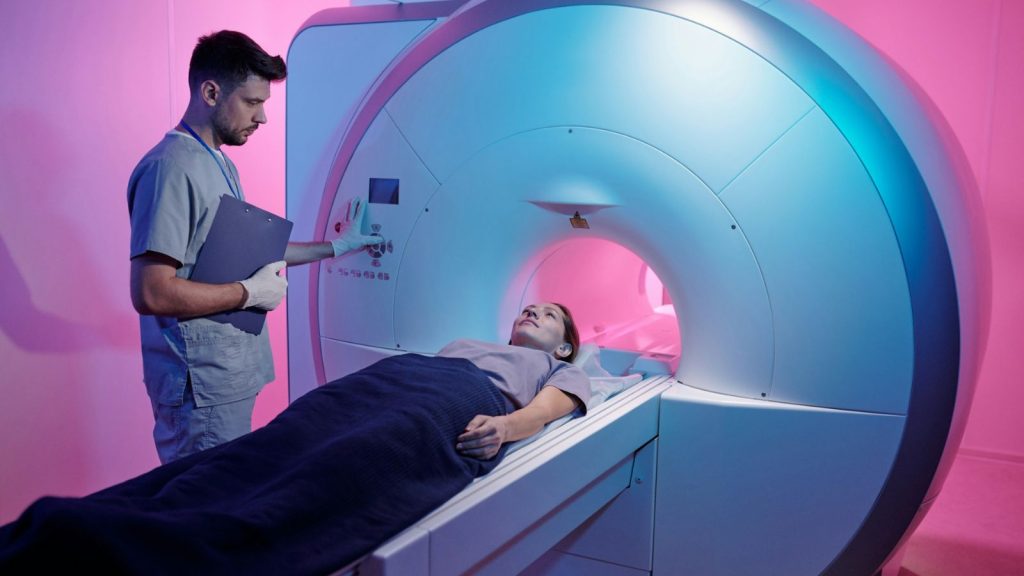 a med tech supervising a woman on a table that slides into the MRI machine