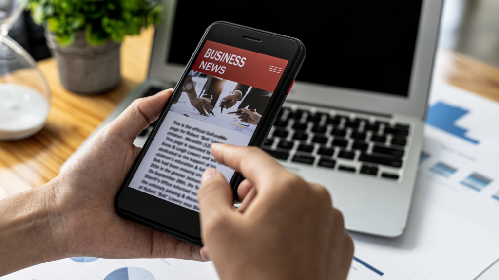 A person holding a smartphone in front of a news website, using a smartphone to read online news via the Internet network