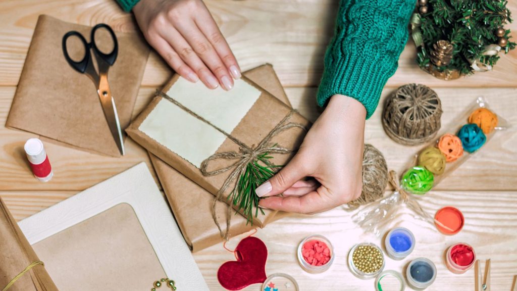 Girl sits at the table wraps Christmas presents.