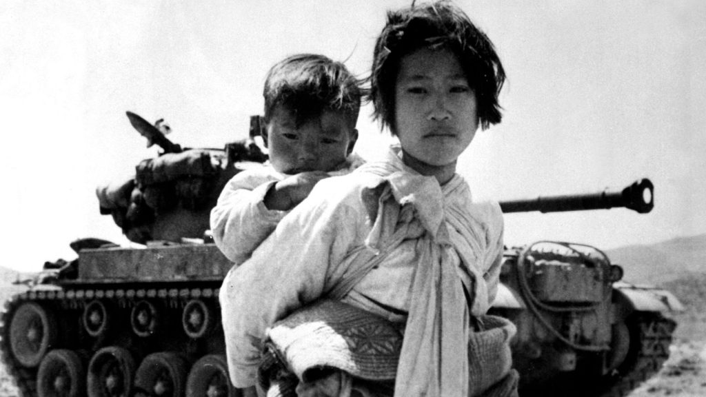 Korean war refugee with a baby on her back and a tank in the background