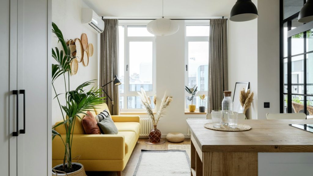 apartment interior in neutral colors with indoor houseplant, mustard couch, table, and rustic decor