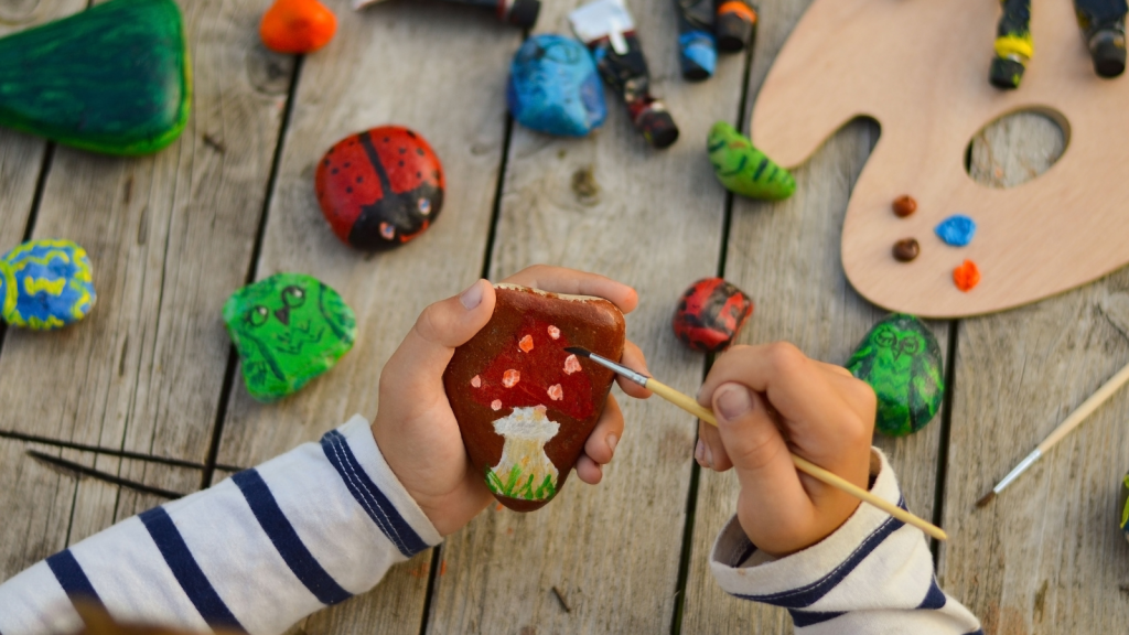 a child's hands drawing a fungus on a stone with acrylic paints