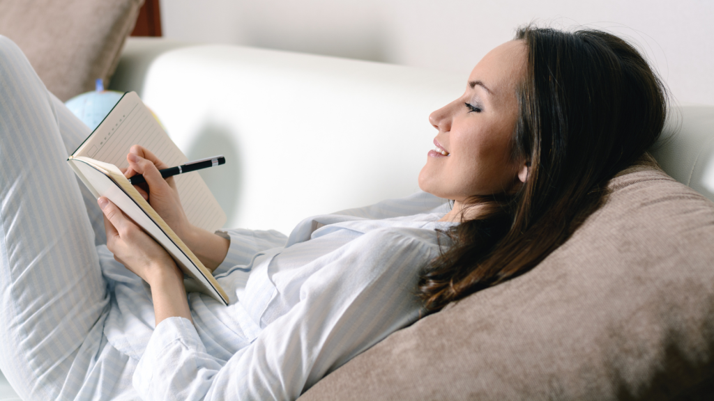 happy smiling girl lying on the sofa in the room and writes a journal